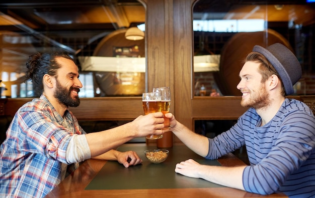 persone, tempo libero, amicizia e concetto di festa - amici maschi felici che bevono birra alla spina al bar o pub e bicchieri tintinnanti