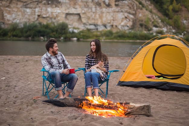 Persone, turismo estivo e concetto di natura - coppia vicino al fuoco del campo in fase di riscaldamento vista dalla tenda.