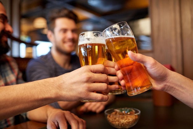 Persone, uomini, tempo libero, amicizia e concetto di celebrazione - amici maschi felici che bevono birra e bicchieri tintinnanti al bar o al pub