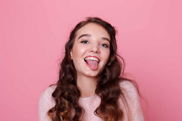 Persone, vacanze, concetto di lusso - Bella giovane donna sorridente in una gonna di pelle nera che presenta qualcosa e guarda la macchina fotografica. studio girato sfondo rosa. Ritratto di una bella ragazza adolescente