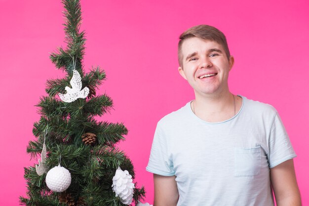 Persone, vacanze e concetto di Natale - giovane uomo sorridente vicino all'albero di Natale su sfondo rosa