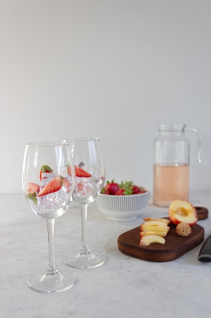 Pesca alla fragola e vino rosato in una caraffa Ingredienti per preparare la sangria estiva Bicchieri con ghiaccio Primo piano Sfondo grigio