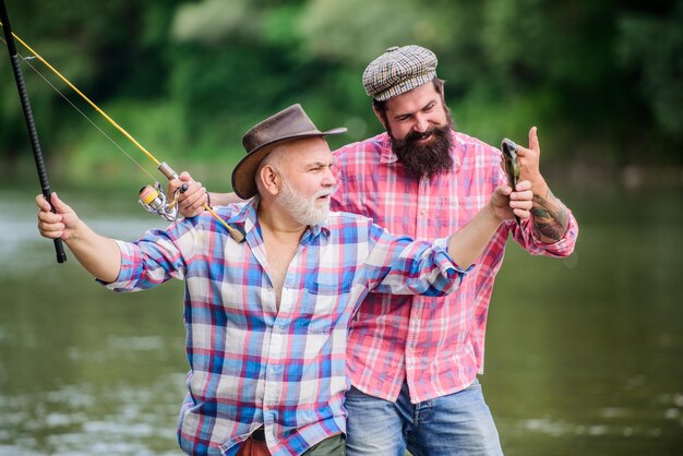 Pesca attività pacifica Padre e figlio pescano Nonno e uomo maturo amici Famiglia di pescatori Rod tackle Attrezzatura da pesca Hobby sport Pesca con mulinello da spinning Soleggiata giornata estiva al fiume