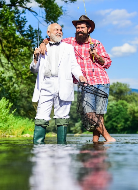 Pesca d'altura padre pensionato e figlio maturo con barba pescatori felici in acqua amici uomini con canna da pesca e rete hobby di pesca pensionamento uomo d'affari Avventure di pesca a mosca