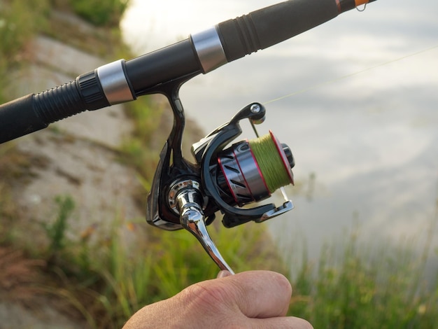 Pesca dell'uomo del primo piano della ruota della canna da pesca sul lago