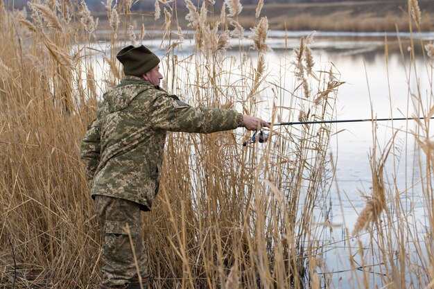 Pesca tra le canne per girare in acque tranquille Un uomo in abiti mimetici con tempo fresco