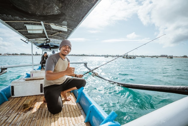 Pescatore asiatico con i pollici in su mentre si tiene una canna da pesca