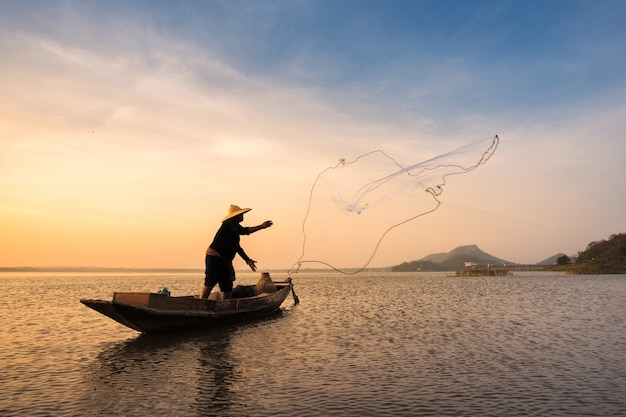 Pescatore asiatico con la sua barca di legno nel fiume della natura al mattino presto prima dell&#39;alba