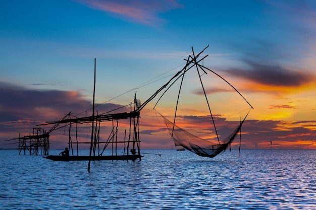 Pescatore asiatico sulla barca di legno con alba