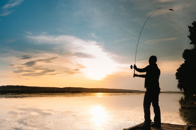 Pescatore che tiene la canna da spinning in riva al lago