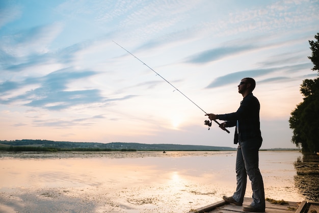 Pescatore che tiene la canna da spinning in riva al lago