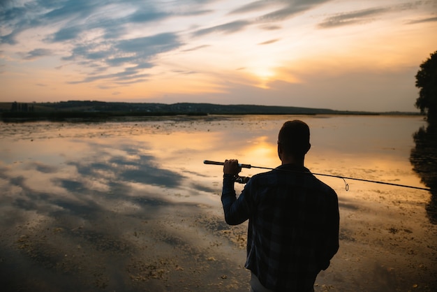 Pescatore che tiene la canna da spinning in riva al lago