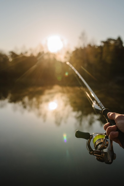 Pescatore con canna da pesca in mano cattura il pesce su una barca Giornata di pesca Filatura in mano sullo sfondo dello stagno