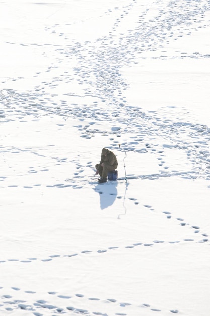 Pescatore di pesca invernale da solo sulla neve