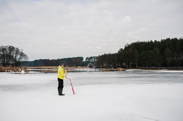 Pescatore invernale che pratica un foro con una vite da ghiaccio Il pescatore perfora la trivella sul lago ghiacciato Pesca invernale sullo stagno