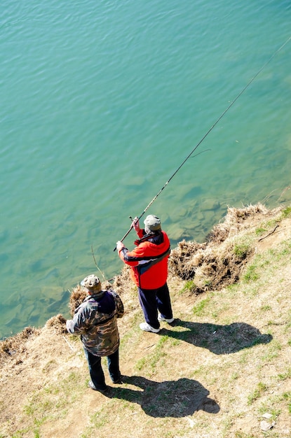 Pescatore seduto con una canna da pesca sulla riva del lago e cattura il pesce