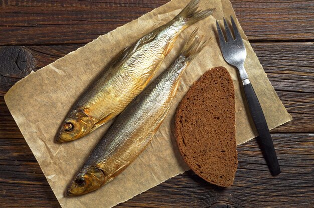 Pesce affumicato con forchetta e pane sul tavolo in legno scuro vista dall'alto