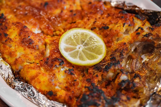 Pesce al cartoccio con limone sul fuoco selettivo del primo piano del piatto bianco