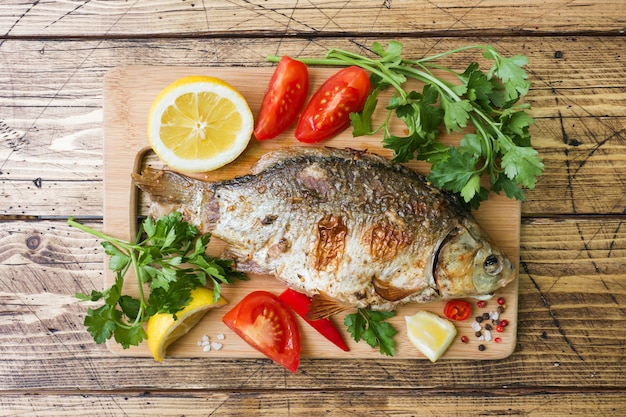 Pesce al forno della carpa con le verdure e le spezie su una tavola di legno.