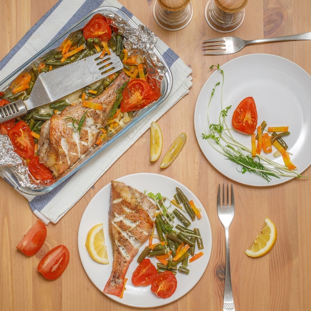 Pesce al forno fresco con verdure servito su piatto su tavolo di legno, vista dall'alto