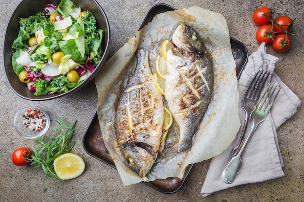 Pesce alla griglia Dorado su carta con limone e rosmarino su grigio