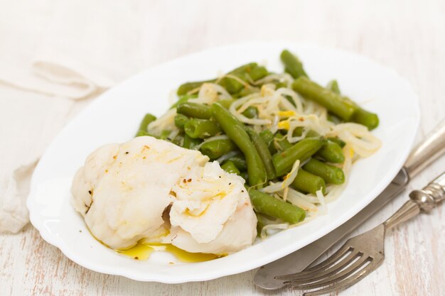 Pesce bollito con fagiolini sul piatto bianco