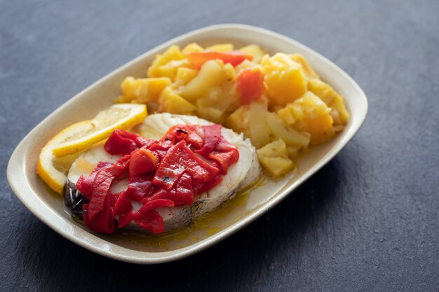 Pesce bollito con pepe rosso, verdure e olio d'oliva sul piatto bianco