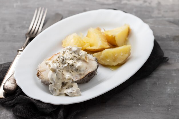 Pesce bollito con salsa tartara e patate lesse sul piatto bianco su fondo in ceramica