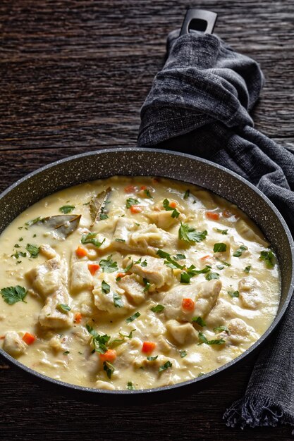 Pesce bollito in salsa a base di latte con verdure, spezie ed erbe aromatiche in padella su un tavolo di legno, cucina inglese