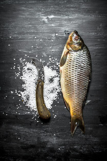 Pesce crudo con sale sulla tavola di legno nera.