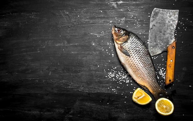 Pesce crudo con un'ascia sulla tavola di legno nera.