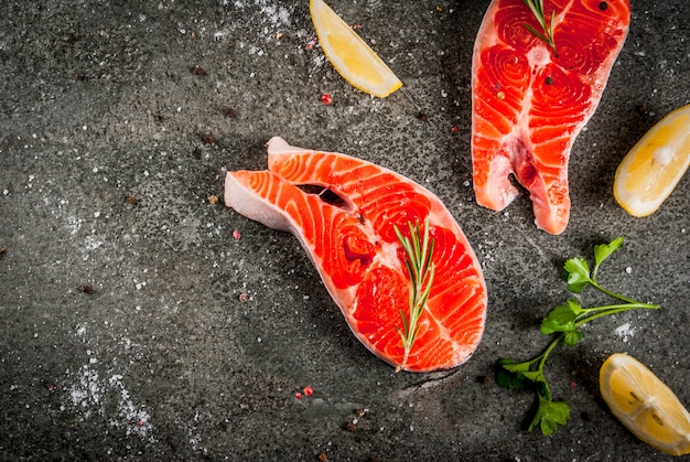 Pesce crudo di salmone fresco con ingredienti per cucinare - olio d'oliva, limone, cipolla, prezzemolo, rosmarino, sul tavolo di pietra nera, copyspace vista dall'alto