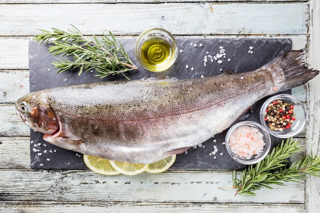 Pesce crudo di trota su ardesia con rosmarino e limone su un tavolo di legno bianco, vista dall'alto