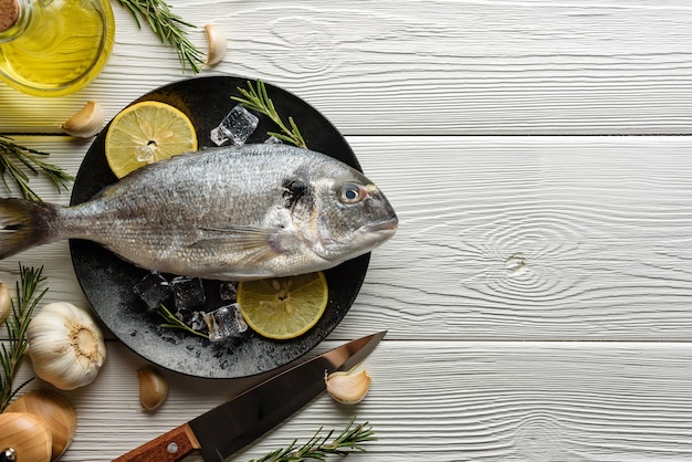 Pesce crudo dorado su un vassoio e ingredienti per la sua preparazione.