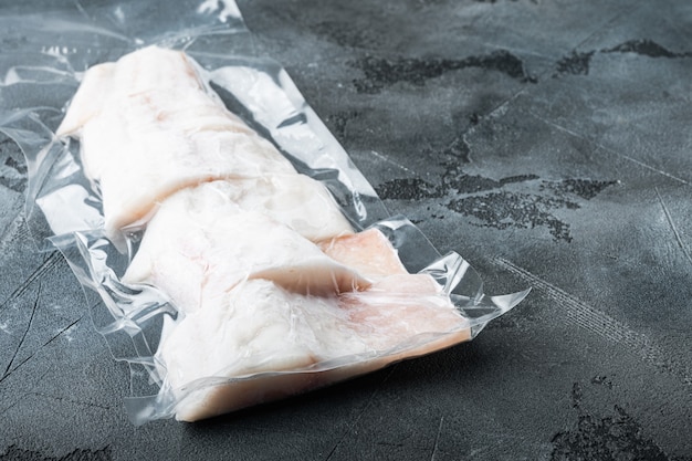 Pesce crudo eglefino senza pelle, confezionato sottovuoto in plastica, sul tavolo grigio