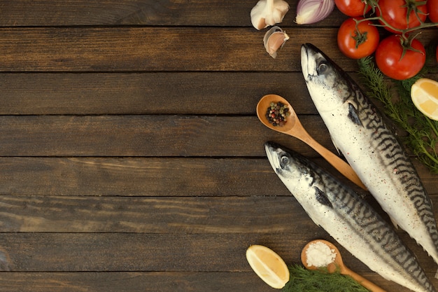 Pesce crudo fresco dello sgombro con il limone, le erbe, l'olio, le verdure e le spezie sul bordo di legno rustico