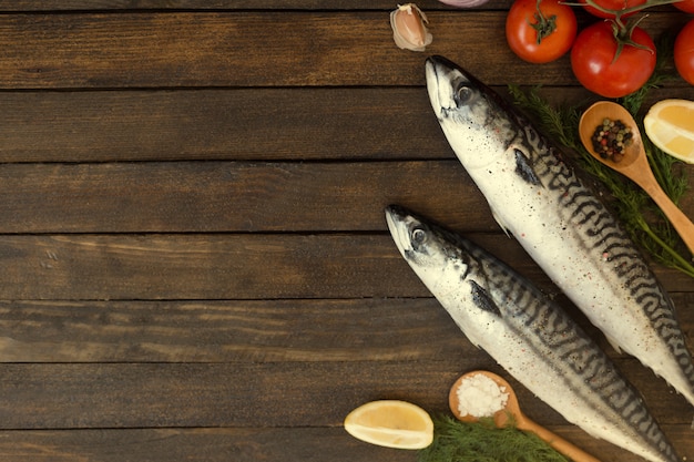 Pesce crudo fresco dello sgombro con il limone, le erbe, l'olio, le verdure e le spezie sul bordo di legno rustico