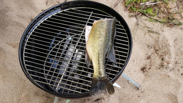 Pesce crudo intero sulla griglia del barbecue a carbone in campeggio in estate Pesca e cucina nella foresta
