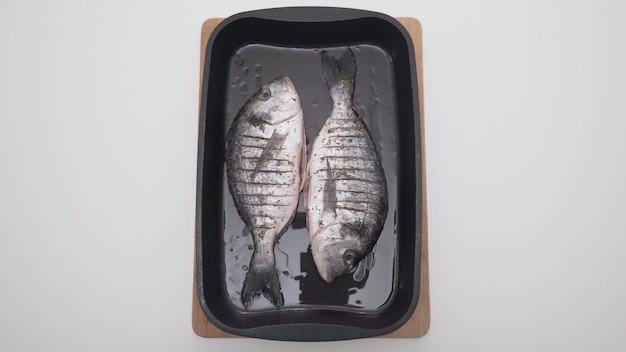 Pesce crudo su foglio da forno su sfondo bianco azione pesce crudo stagionato su padella all'olio prima della cottura in
