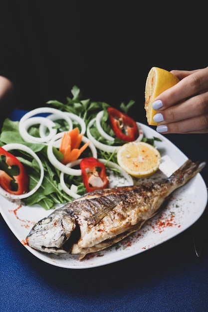 Pesce cupra fritto di orata su piatto bianco con rucola di cipolla e fette di limone