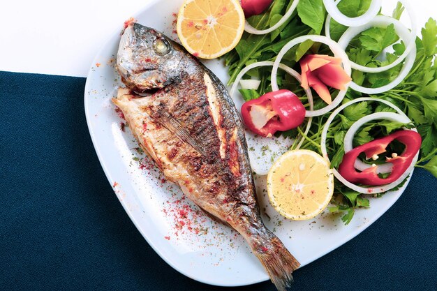 Pesce cupra fritto di orata su piatto bianco con rucola di cipolla e fette di limone