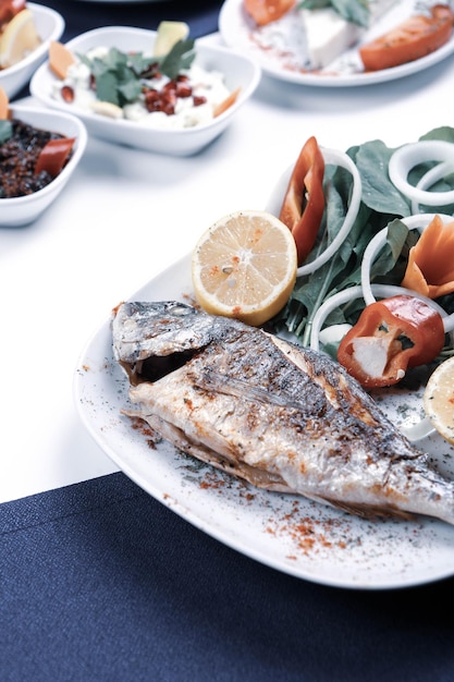 Pesce cupra fritto di orata su piatto bianco con rucola di cipolla e fette di limone