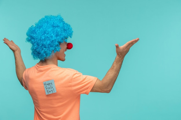 Pesce d'aprile ragazzo pagliaccio sorridente agitando le mani capelli blu blu post-it adesivo nota divertente naso rosso