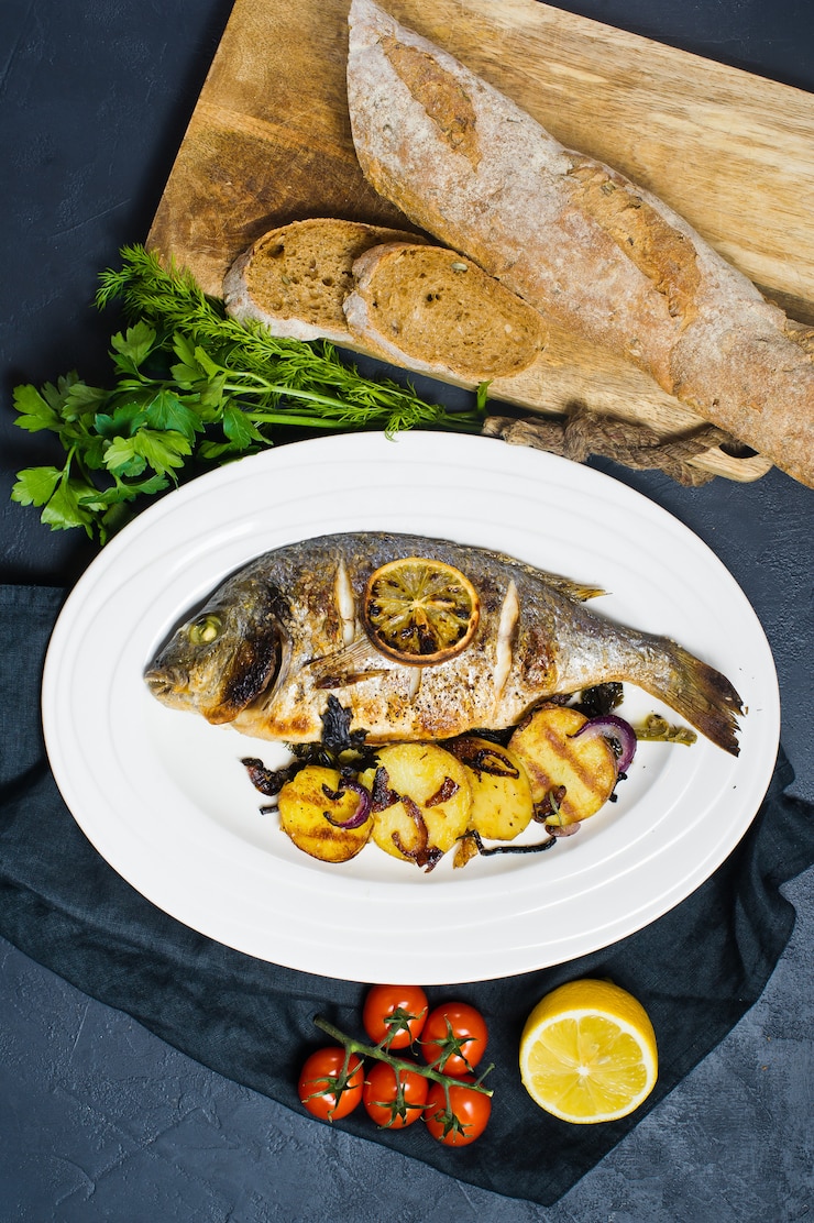 Foto pesce dorado al forno su un piatto bianco, guarnire le patate fritte.