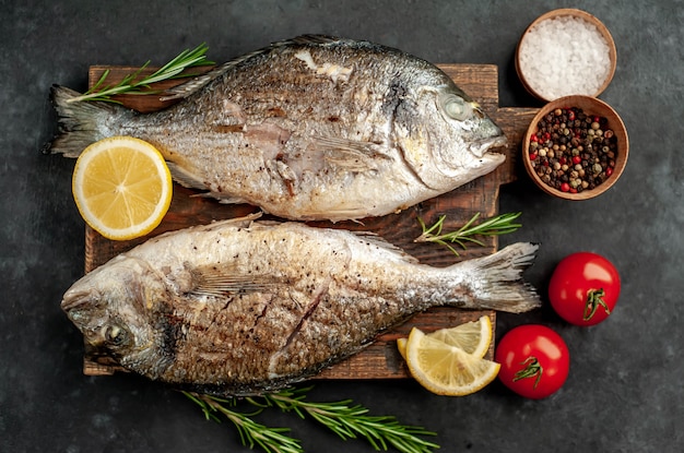 pesce dorado alla griglia su un tagliere con spezie e limone su uno sfondo di pietra