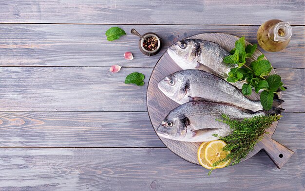 Pesce dorado crudo con erbe verdi che cuocono sulla tavola da taglio