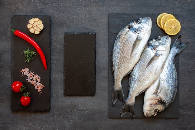 Pesce dorado fresco con spezie aglio limone e condimento su tagliere nero sul tavolo