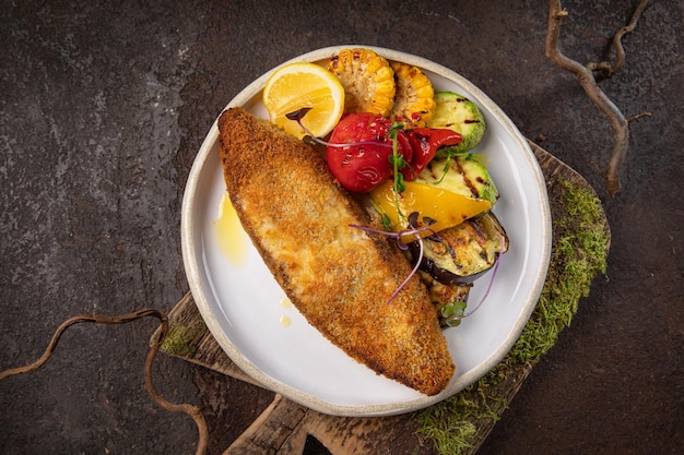 Pesce e filetto di pesce fritto piatto bianco e verdure su sfondo nero