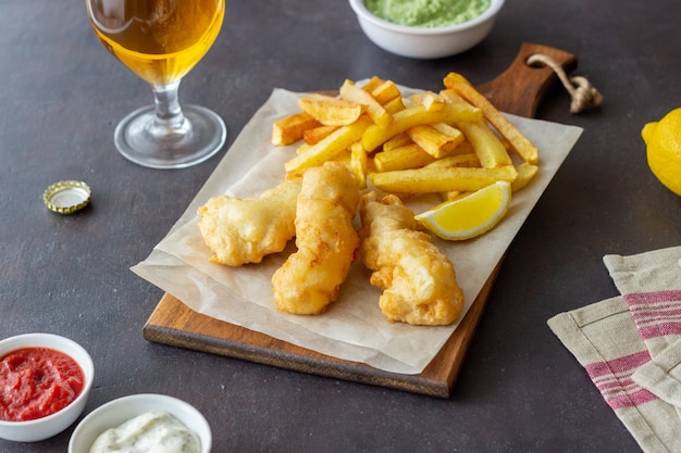 Pesce e patatine fritte su una superficie scura. Fast food britannico. Ricette. Snack alla birra. Cucina britannica tradizionale.