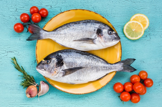 Pesce fresco di dorado sul piatto giallo e verdure su fondo blu. Vista dall'alto.